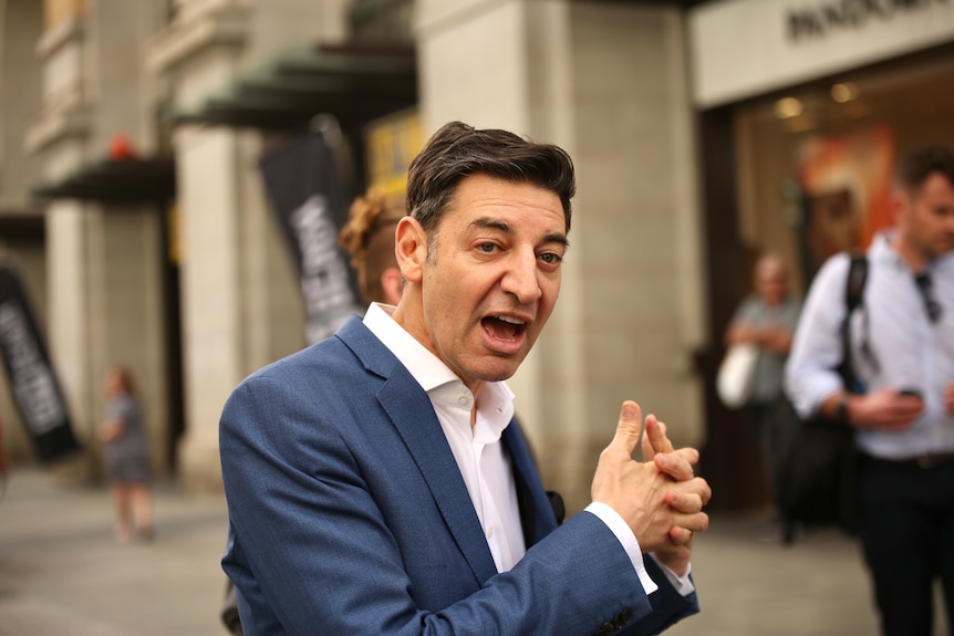 Un uomo vestito di blu cammina per Murray Street, parlando, con le mani giunte.