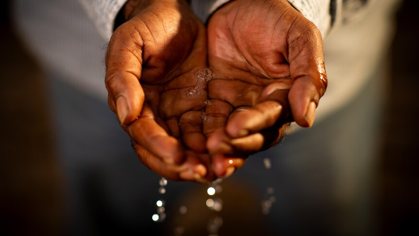 A close up of a pair of hands scooping up water