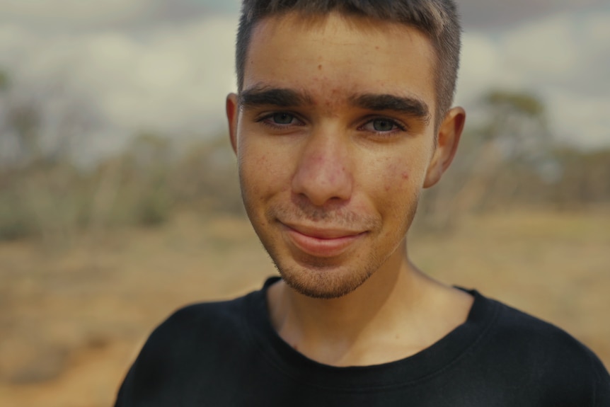 A young man looks at the camera. He's smiling and looks comfortable and sure of himself.