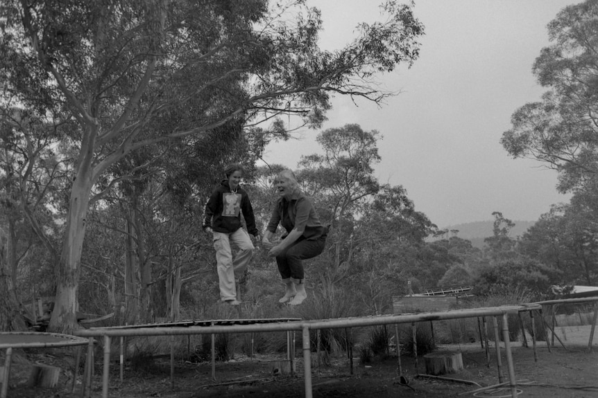A woman and girl jump on a trampoline surrounded by other trampolines. 