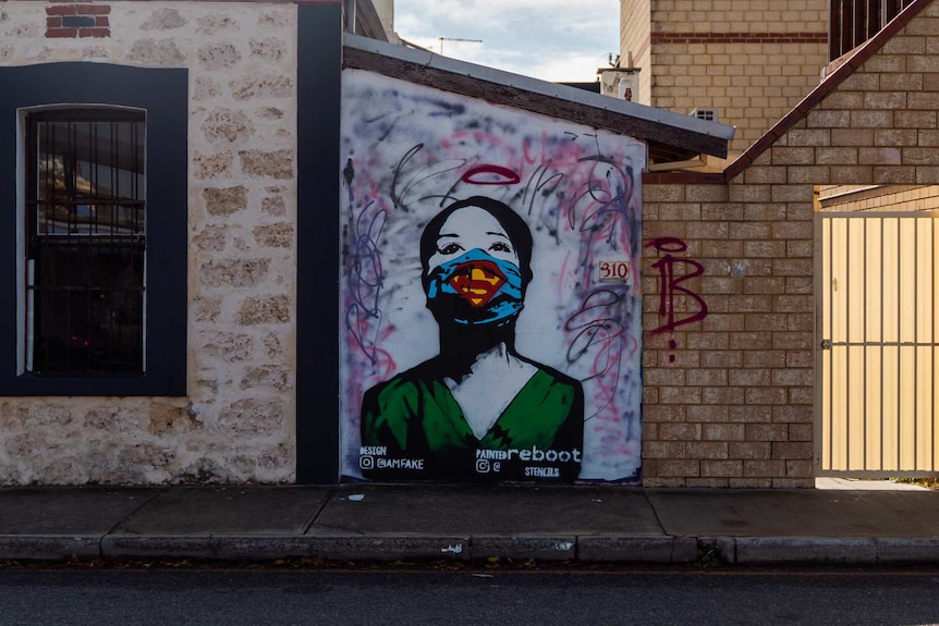 A stencil painting of a woman wearing a superhero face mask on the side of a building wall