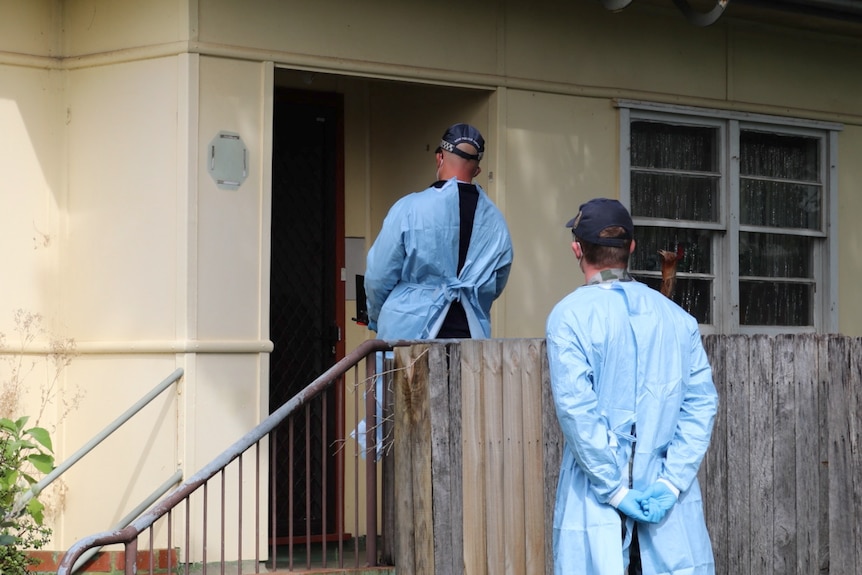 Two people in full PPE at the door of a house.