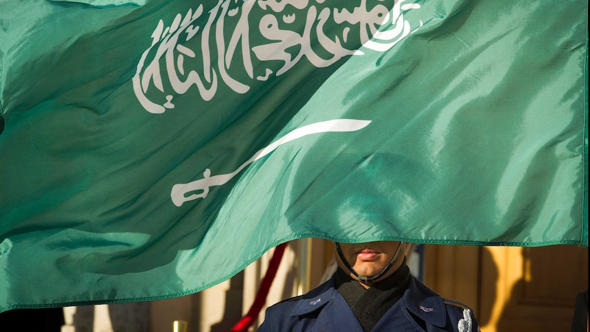 An Honour Guard member is covered by the flag of Saudi Arabia.