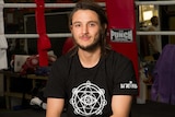 Portrait of a male martial arts champion in a black T-shirt sitting inside a fighting ring.