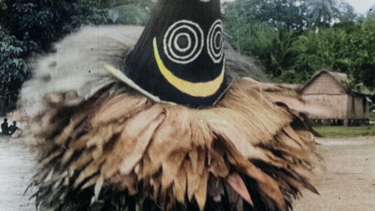 A person in the middle of the village wearing a full body costume that has a cone shaped mask over their head.