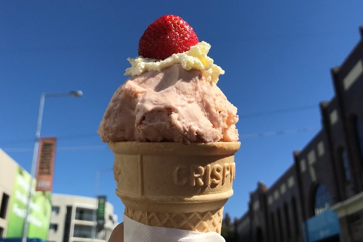 Close-up of a delicious strawberry on top of a squirt of whipped cream sitting on a scoop of strawberry ice-cream in a cone
