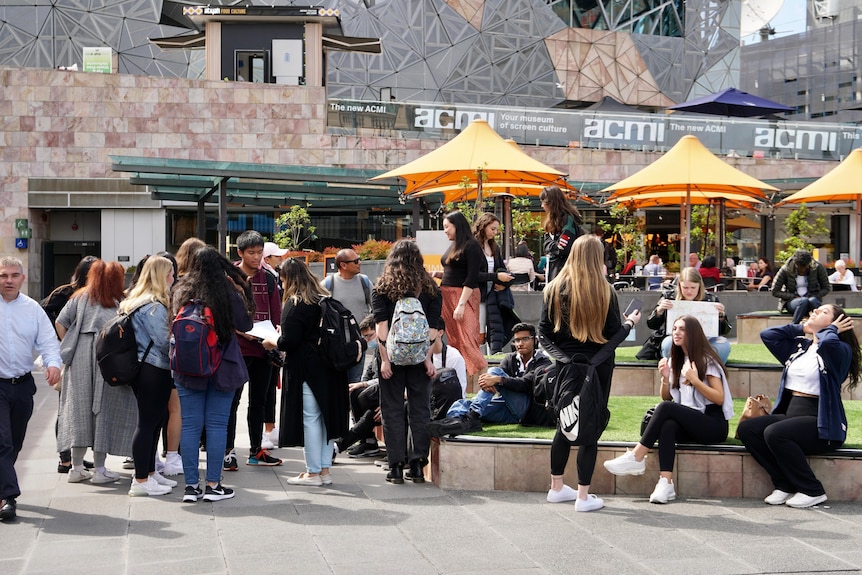 A group of people stand on a sunny day in Melbourne's Federation Square.