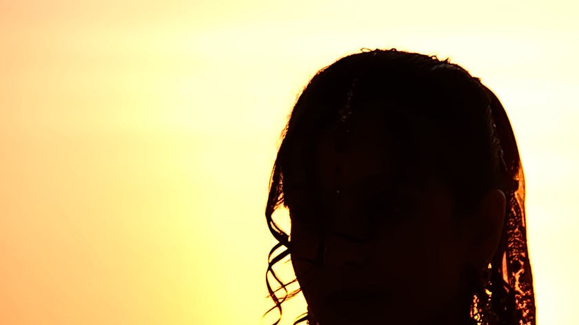 A woman's head is silhouetted against a light background, with a hint of a veil.