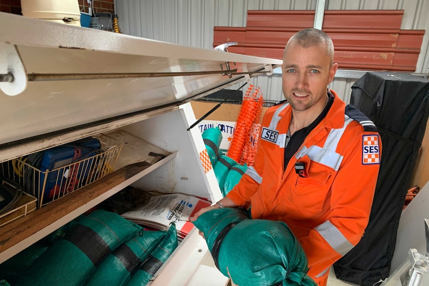 An emergency services worker wearing orange hi-vis lifts a sandbag into a trailer.