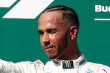 Lewis Hamilton stands on the podium and squints into the sun, giving fans the thumbs up