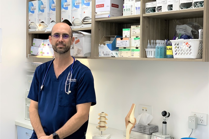 A doctor dressed in scrubs standing in front of a shelf of medical supplies