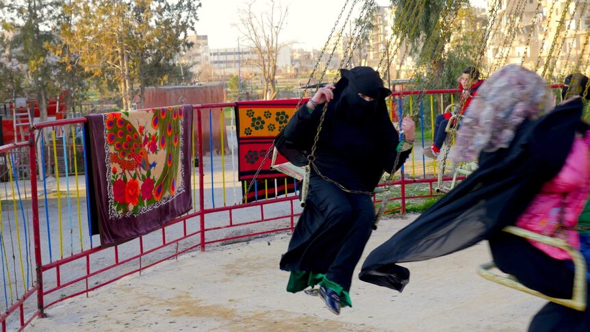 A girl in a burqa rides on a swing on a merry-go-round