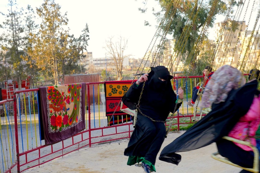 A girl in a burqa rides on a swing on a merry-go-round
