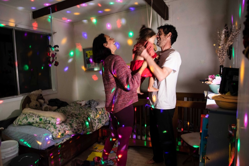Mary, her partner Chris and young daughter Amaya laughing and having a dance party in Amaya's bedroom.
