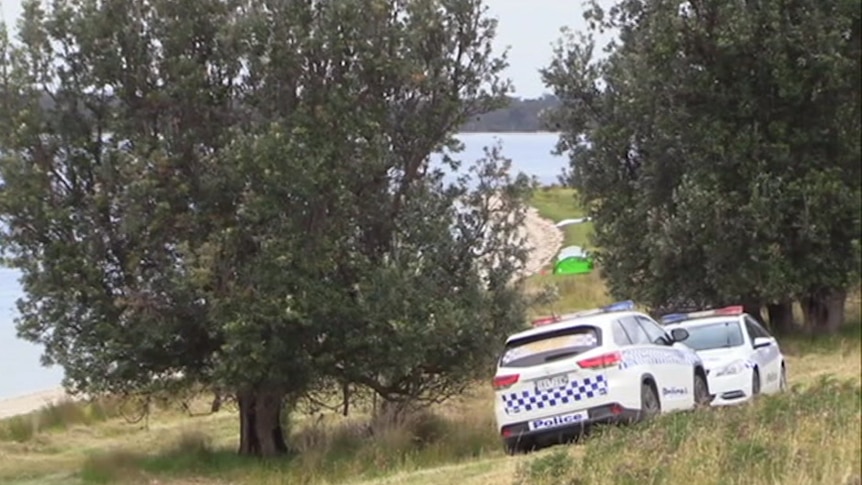 Police vehicles parked at the edges of a lake, with a small tent pitched on the shore.