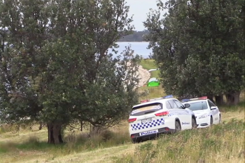 Police vehicles parked at the edges of a lake, with a small tent pitched on the shore.