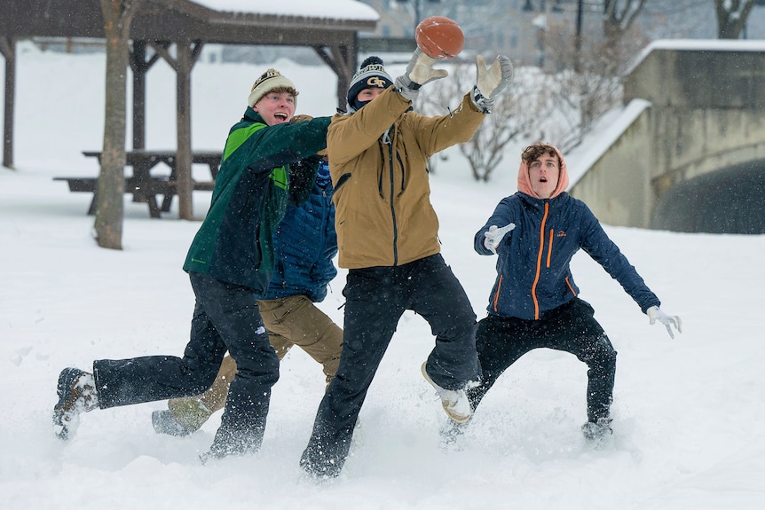 Four teen boys play with an American football in a snowy park