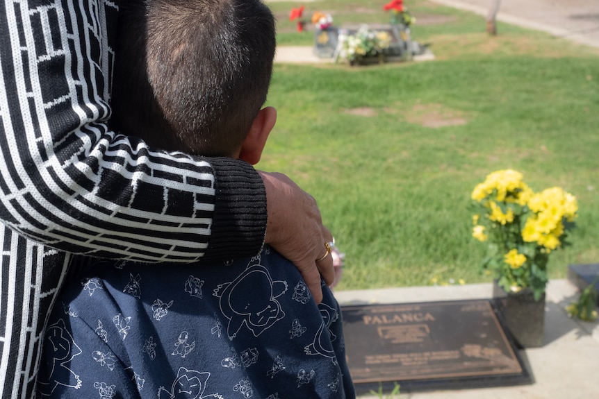 A woman with her arm around a child near a grave.