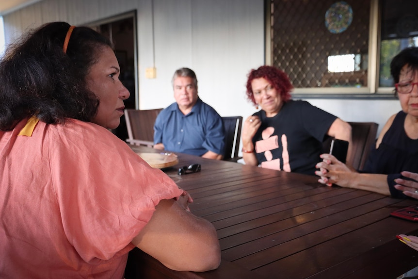 A woman sits at a table with friends in the background.