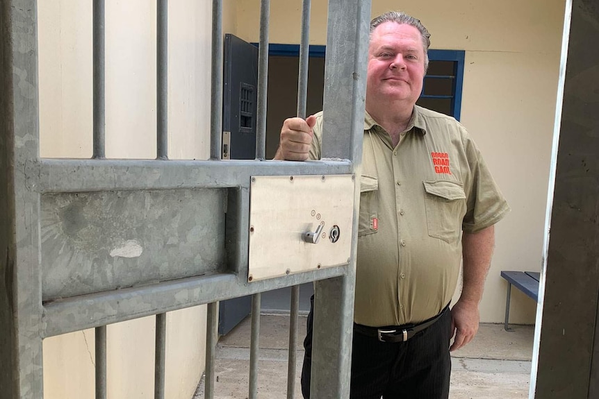 Tour director Jack Sim stands holding the cell door in Brisbane's old Boggo Street Jail.