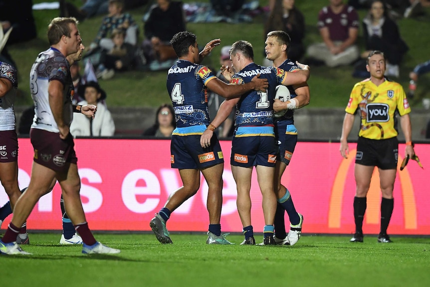 An NRL player holding the ball celebrates with his teammates after a try.