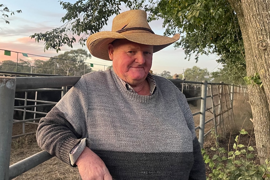Man with a cattle hat leans smiling against a rail