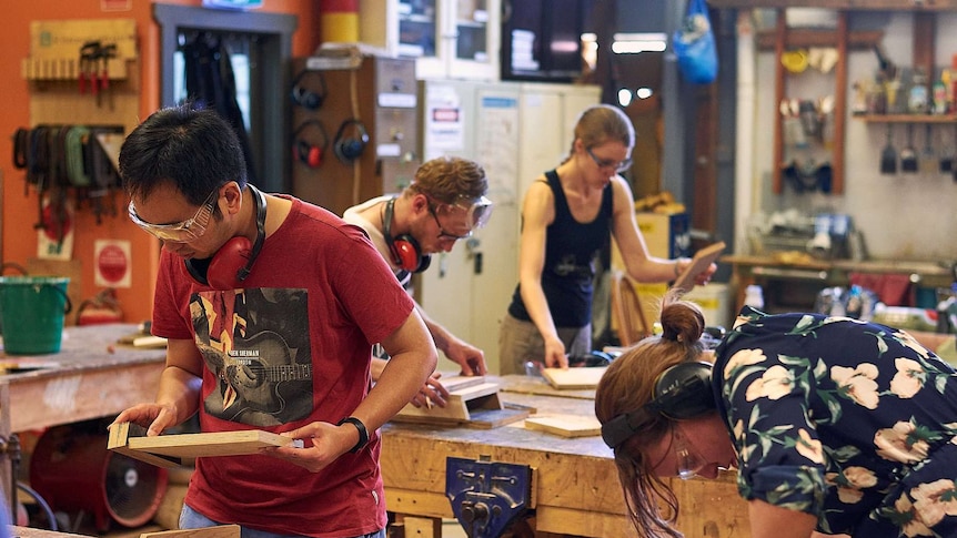 A group of people stand in a workshop wearing personal protective equipment working on wood products.