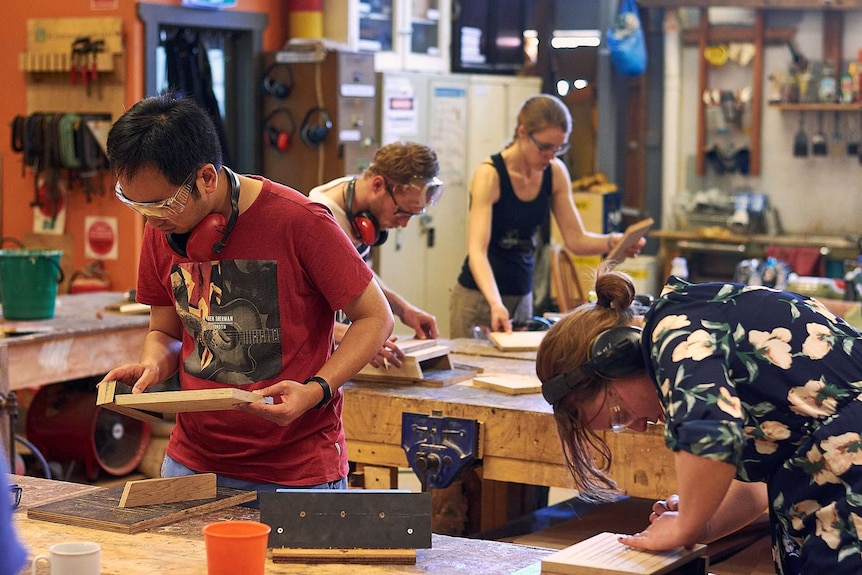 A group of people stand in a workshop wearing personal protective equipment working on wood products.