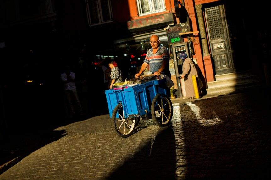 A food street vendor pushes his trolley across cobblestones.