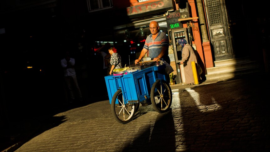 A food street vendor pushes his trolley across cobblestones.