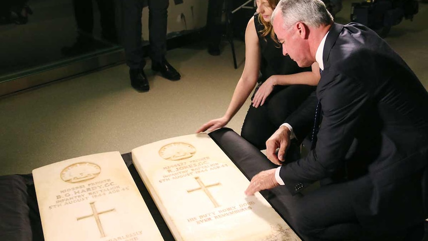 Two people crouch over two headstones laid out on black fabric.