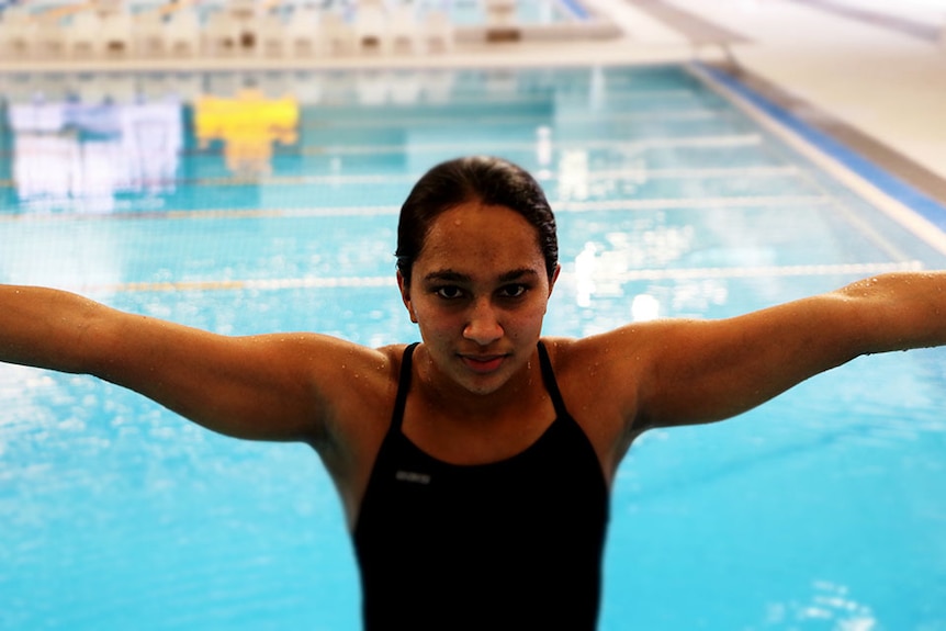 Woman with arms outstretched with her back to an indoor pool.