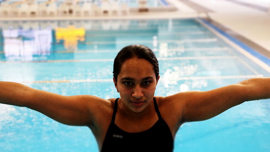 Woman with arms outstretched with her back to an indoor pool.