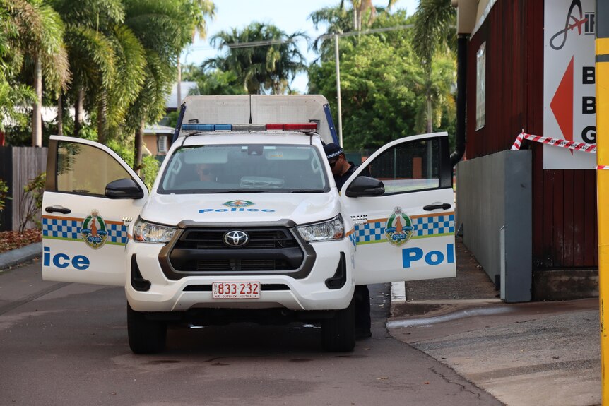 A NT Police 4WD parked on the curb, with all its doors open and several officers milling around.