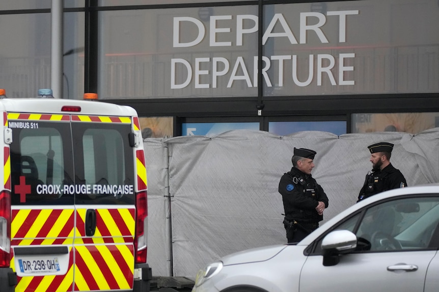 Two policemen standing outside a closed off building with a departure sign 