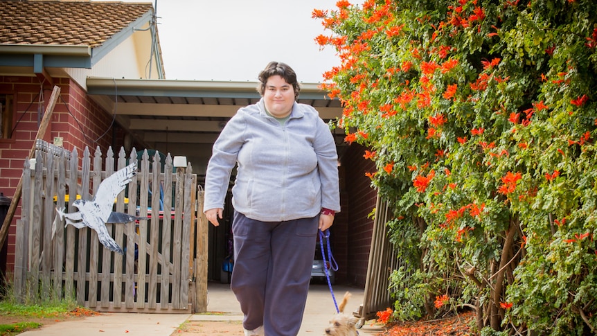 Dee Coulls walking down her driveway with assistance dog Bubba on a lead.