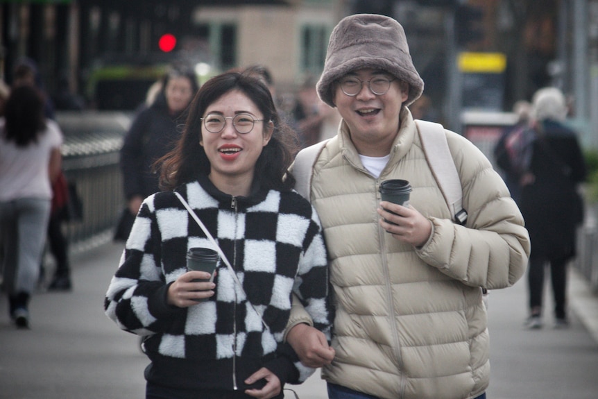 Two people wearing winter clothes smile as they walk in Melbourne CBD.