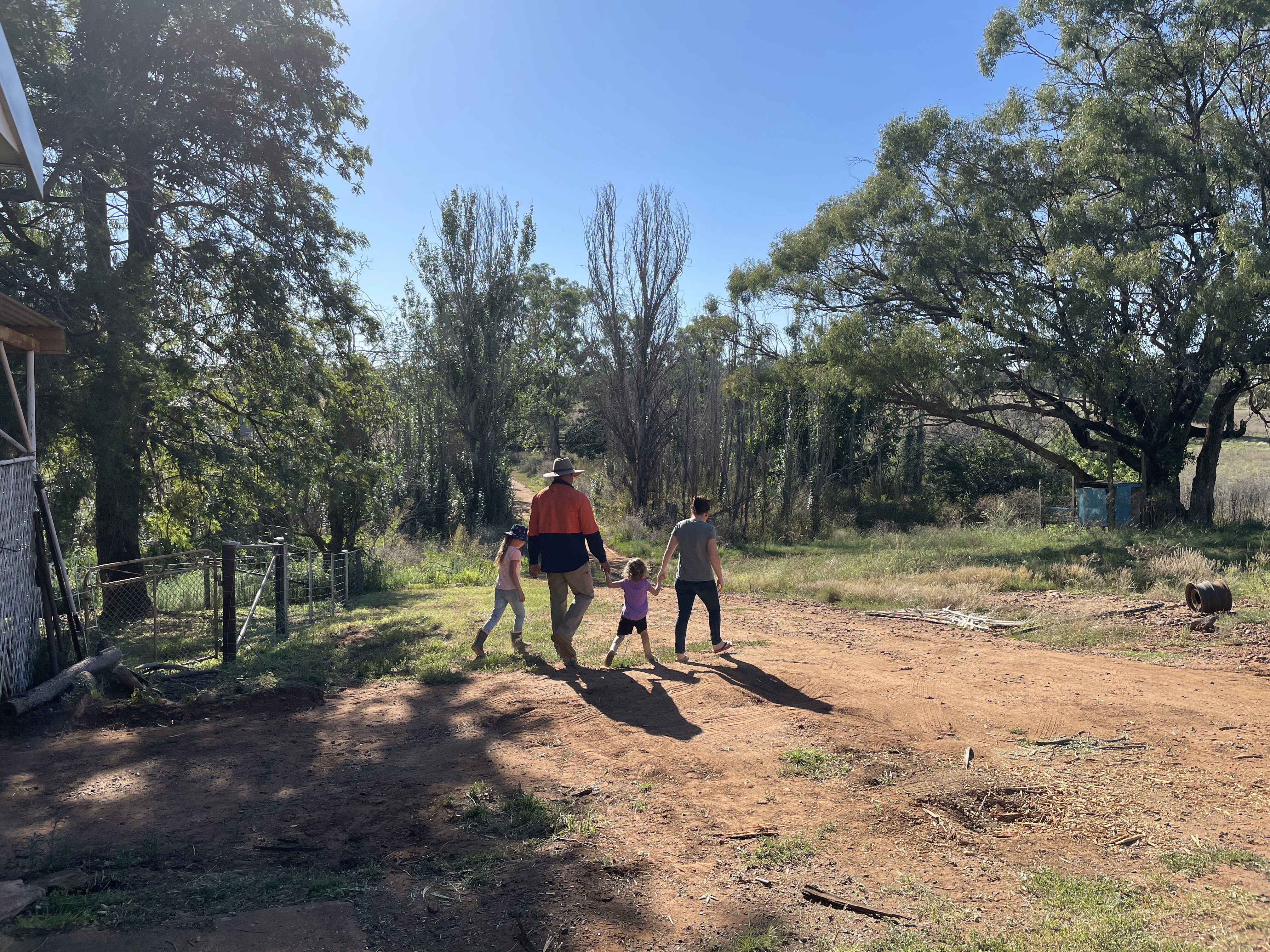 Two adults and two children hold hands and walk towards the bushland.