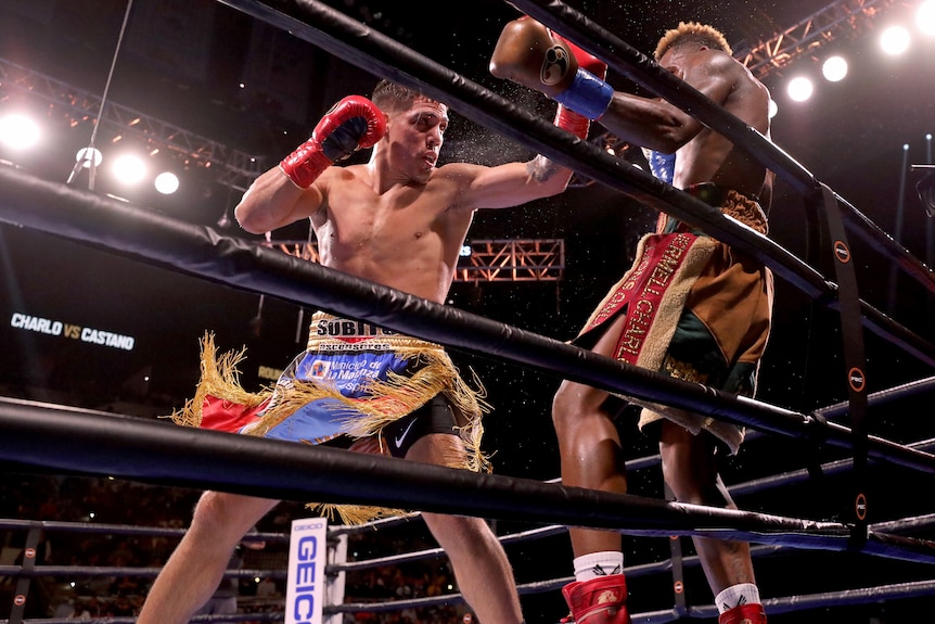 A boxer swings with his left hand at his opponent on the ropes during a boxing match.