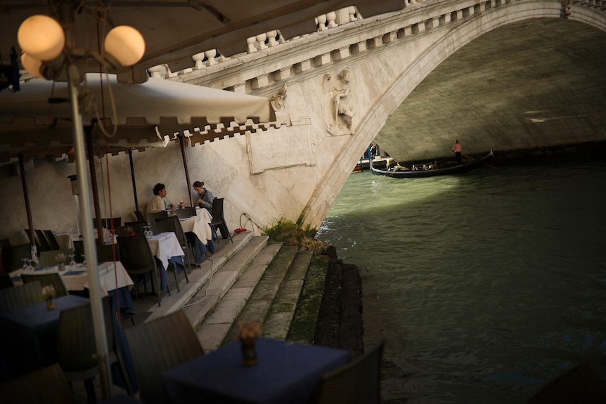 Tourists eat a meal on an almost empty restaurant terrace in Venice.