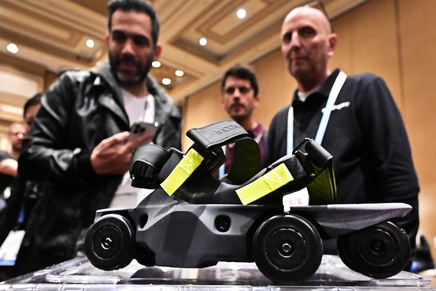 A close up of a sandal-like shoe with velcro straps, a thick base and small wheels. People look down at it from above