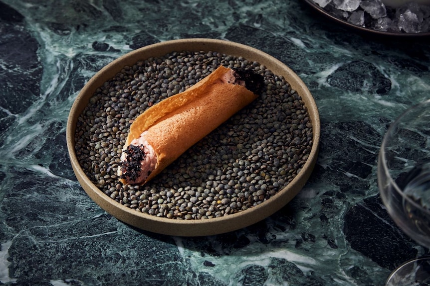 A cannoli filled with cultured quail cell parfait on a dark plate and counter. 