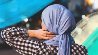 Woman wearing a purple hijab looking out at a street in the evening, with brush strokes around her.