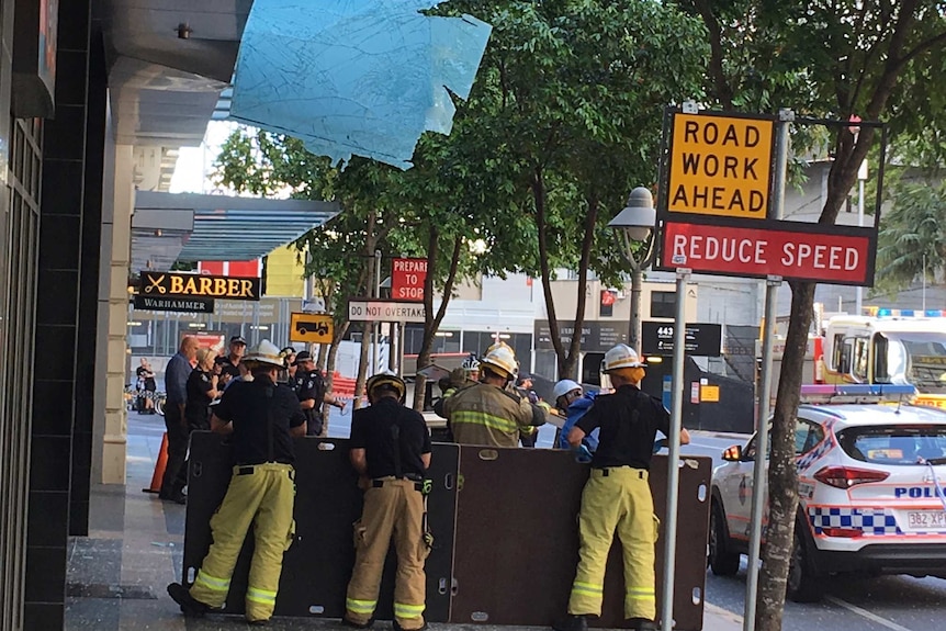 A glass panel at the Aurora building hanging down with fire crews standing around.