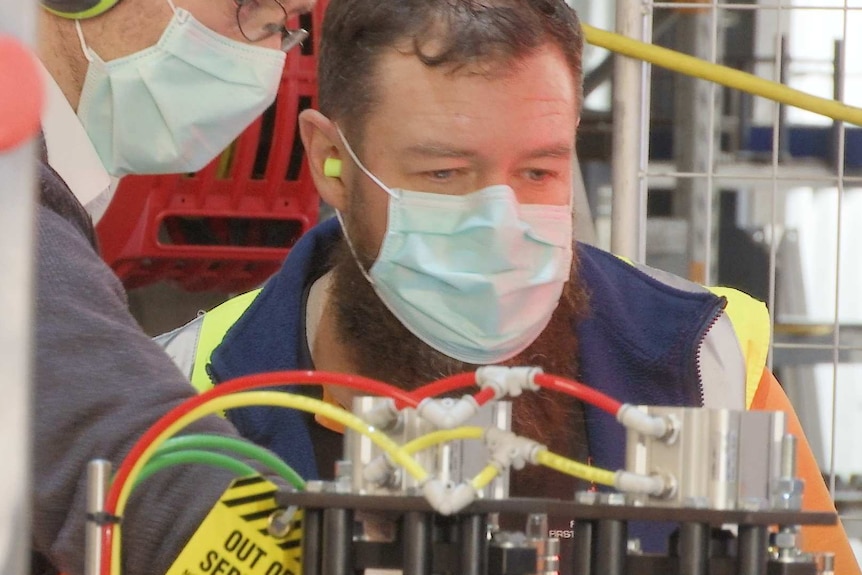 A bearded worker in high vis looks closely at one of the machines being built.