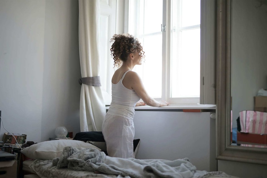 Woman looking out her window in a messy room