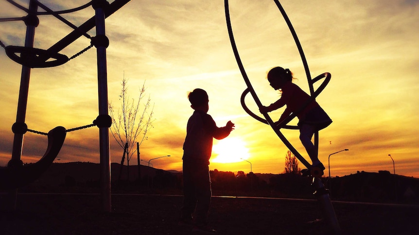 Children playing on playground equipment at sunset.