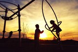 Children playing on playground equipment at sunset.