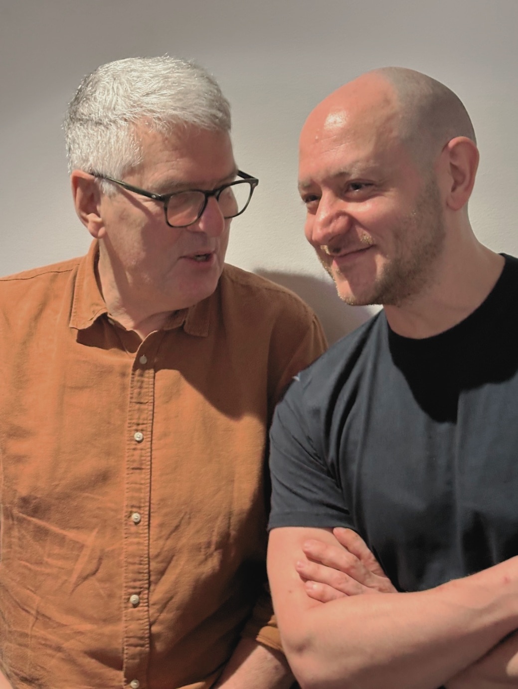 Two men look at each other in front of a grey background