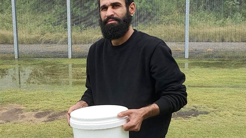 Amin Afravi collects rainwater in a bucket at the Brisbane's Immigration Transit Accommodation.